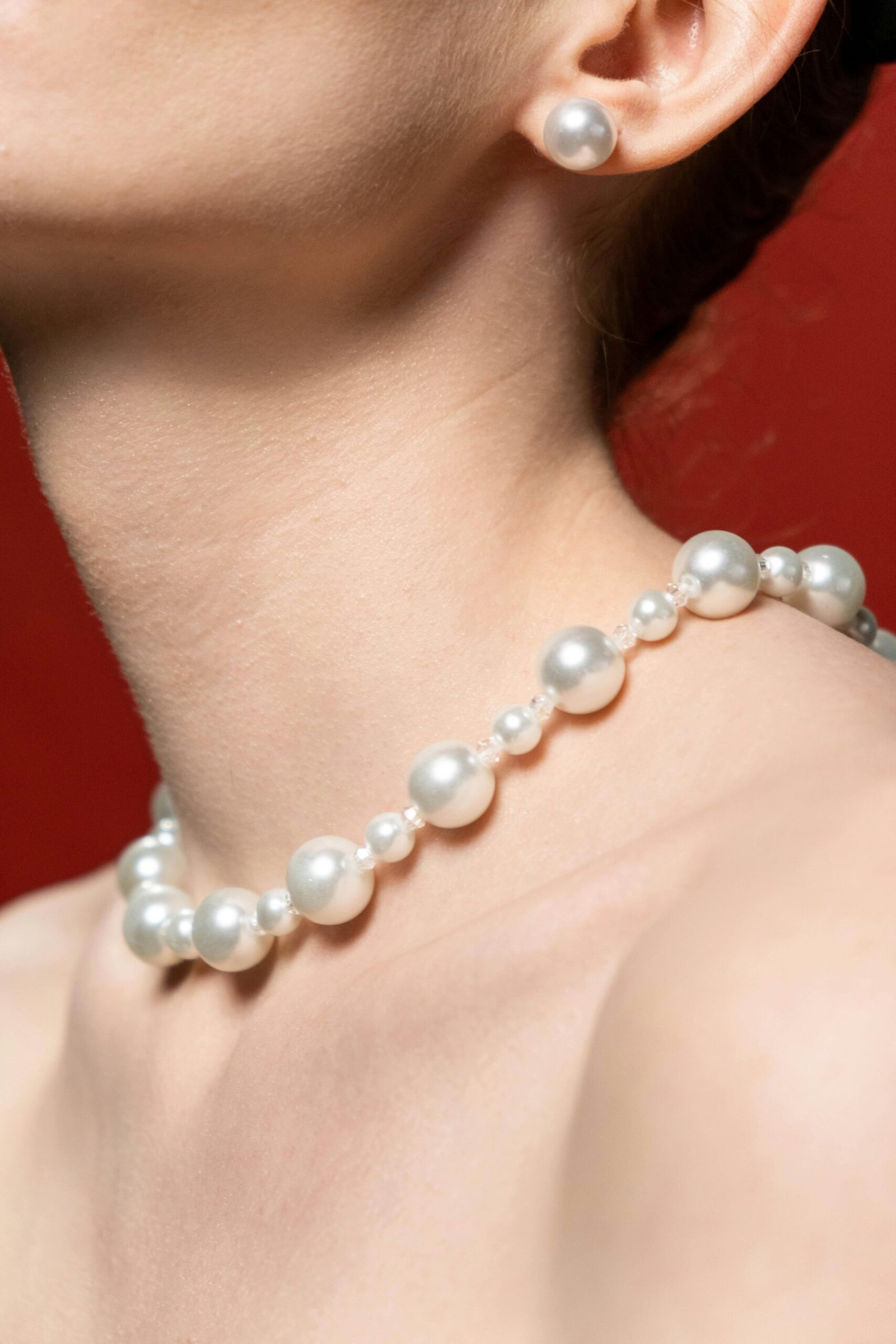 Close-up of a woman's neck adorned with a pearl necklace against a red background.
